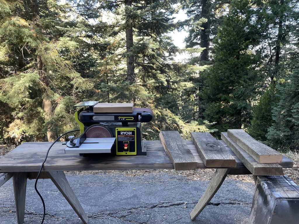 Belt sander on an outdoor bench with pines behind