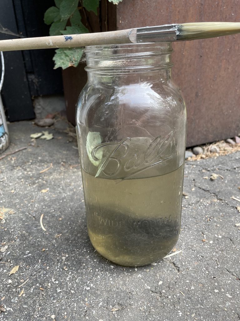 Ball jar of homemade vinegar and steel-wool stain with a brush across it